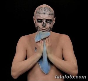 Фото татуировки на лице мужчины, имитирующей череп и маску, с добавлением голубого галстука, создающее сюрреалистичный и провокационный эффект.